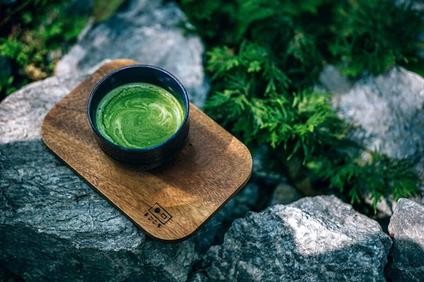 Cup of matcha tea on wooden board on rock outside