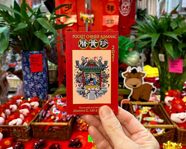 Chinese pocket almanac held in front of Lunar New Year display