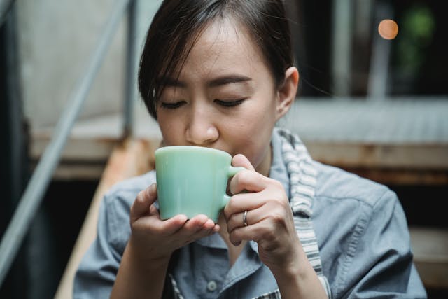 Woman in blue shirt drinking mug of warm beverage