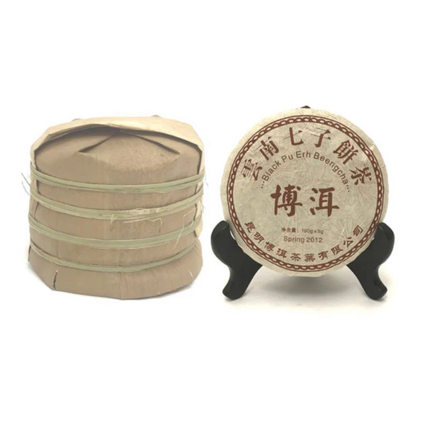 Yunnan Chi Tse Pu Erh compressed tea. One on a stand. It is next to a pile of the tea cakes stacked on top of each other