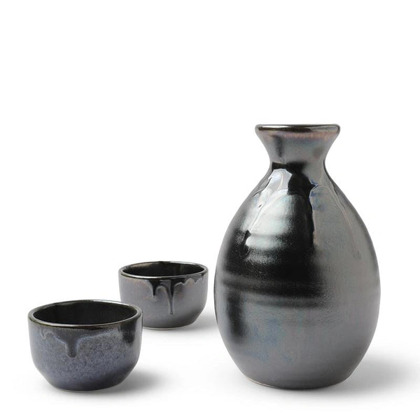 Three-piece ceramic sake set featuring a large bottle and two small cups in a glossy dark charcoal glaze with subtle blue undertones and dripping glaze details, set against a plain white background.