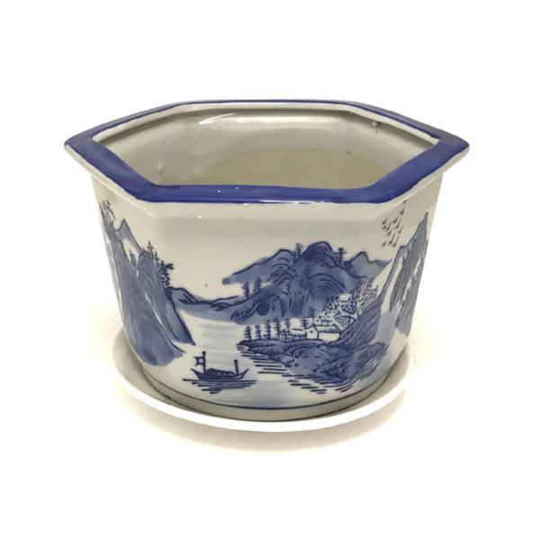 Hexagonal blue and white flower pot on a white flower pot tray. The flower pot has a landscape painted on it