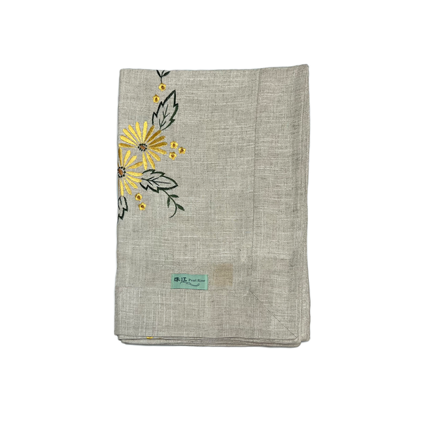 Folded flax tablecloth with embroidered yellow flowers and green leaves on a white background