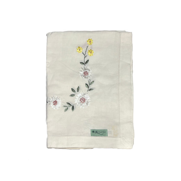 Folded beige tablecloth with floral embroidery on a white background