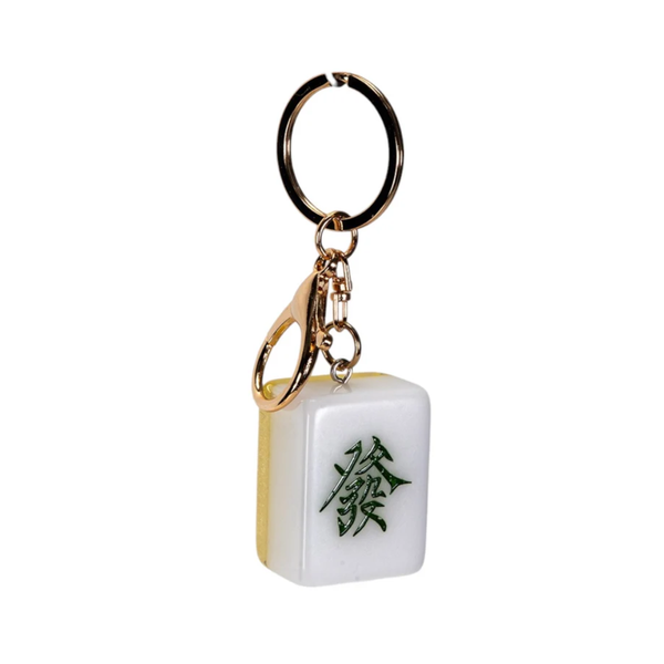 A novelty keychain shaped like a white mahjong tile with a green Chinese character for '发' (meaning 'luck' or 'shoot'), attached to a gold-tone split ring and clasp, shown on a plain white background.