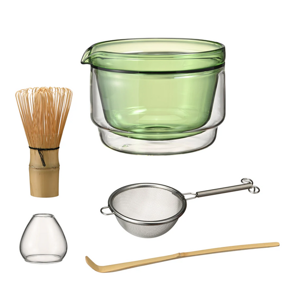 Set of tea-making tools including a green glass bowl, whisk, small vase, strainer, and wooden spoon on a white background.