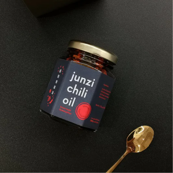 Jar of junzi chili oil with a gold spoon on a black background