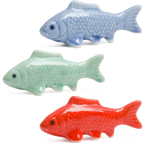 Three glossy ceramic fish-shaped objects in light blue, mint green, and bright red, arranged vertically on a white background.