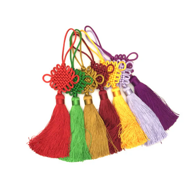 Six Chinese knot tassels next to each other. The colors from left to right are red, green, gold, burgundy, yellow, lavender and purple