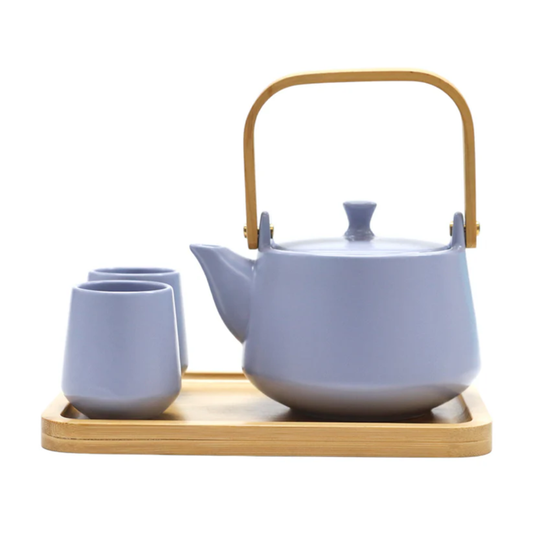 Ceramic teapot with wooden handle and matching cups on a wooden tray against a white background
