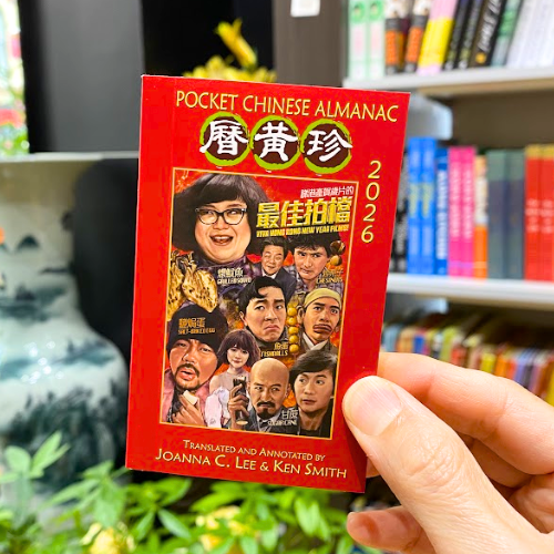 Someone holding the 2026 Pocket Chinese Almanac with plants, vase, and books in the background