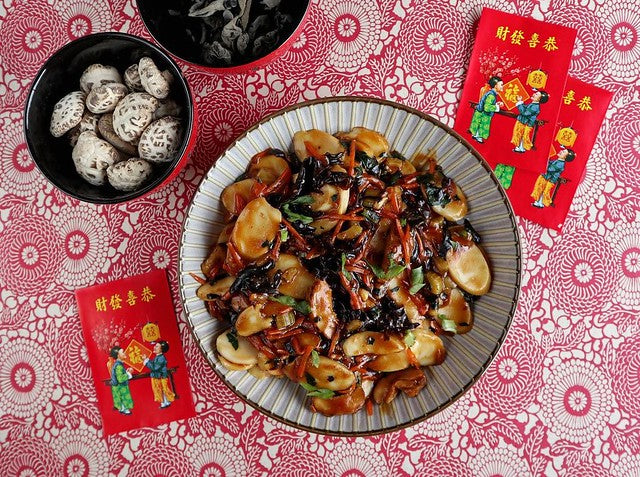 White bowl with rice cakes surrounded by red envelopes on red and white background