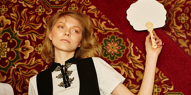 White female model lying on rug holding a fan