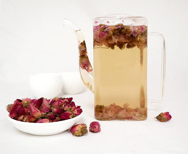 White dish of pink rosebuds beside glass pitcher of rosebud tea
