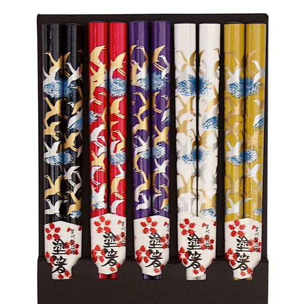 Five pairs of chopsticks, each pair featuring a different color scheme with white cranes and blue wave motifs. The chopstick colors include black, red, purple, white, and gold, with white handles decorated with red cherry blossoms and black kanji characters.