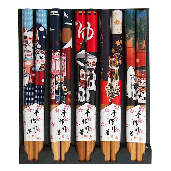A set of five decorative chopsticks, each featuring a different colorful Japanese-style illustration including cats, stars, waves, and cherry blossoms, with white paper bands displaying Japanese text near the wooden handles.