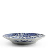 A round white ceramic plate with intricate blue floral and scroll patterns, photographed against a seamless white background.