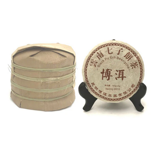 Yunnan Chi Tse Pu Erh compressed tea. One on a stand. It is next to a pile of the tea cakes stacked on top of each other