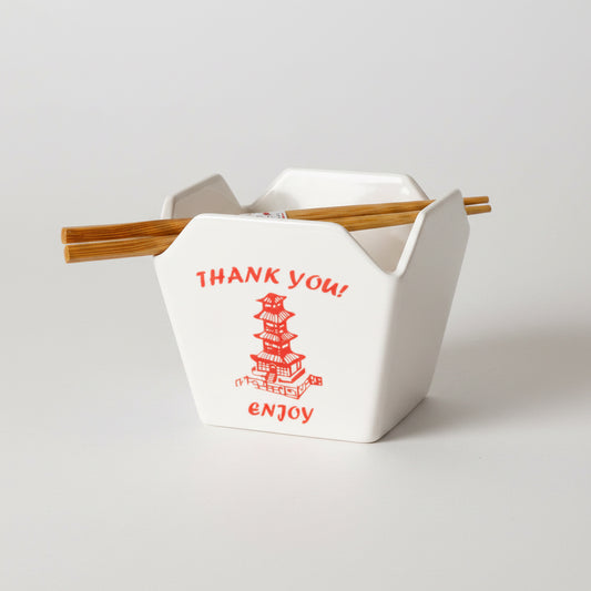 A white ceramic chopstick holder with red printed text reading 'THANK YOU!' and 'enjoy' alongside a red pagoda illustration, shown with two wooden chopsticks resting across the top on a white background.