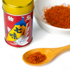 Red spice can with yellow lid, wooden spoon with spice, and white bowl of spice on a white background