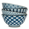 A stack of four blue and white ceramic bowls, each with a unique geometric pattern: starburst, stripes, hexagons, and checkerboard. The mood is elegant and refined.