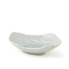 A small, shallow ceramic dish with a leaf-like organic shape, featuring a glossy off-white glaze with subtle light blue-green undertones and a small footed base, set against a plain white background.
