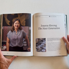 An open book spread held by two hands, showing a printed essay about Joanne Kwong with a portrait photo and text on the right page, against a light neutral background.