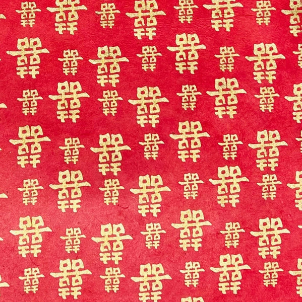 Red paper with a repeating pattern of gold Chinese double happiness symbols.