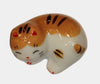 Ceramic cat-shaped object with white body and brown and black pattern on a white background.