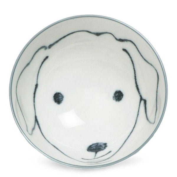 A white ceramic bowl with a minimalist dog face design, featuring simple outlines for ears and features. The tone is playful and charming.