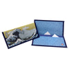 A folded Japanese-style wallet featuring Hokusai's Great Wave off Kanagawa artwork. One is shown closed with the wave illustration on a muted yellow-green background, and another is shown open to reveal a blue starry sky with white mountain peaks.