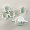 White ceramic teapot and four matching cups with fish design on a light wooden surface