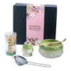 Ceremonial matcha set with green bowl, whisk, and other tools in front of a decorative box.