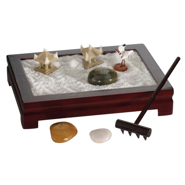 Close up of mini zen garden with sand, small gazebos, crane, three stones, and one small rake