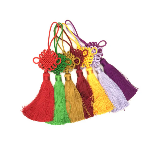 Six Chinese knot tassels next to each other. The colors from left to right are red, green, gold, burgundy, yellow, lavender and purple 