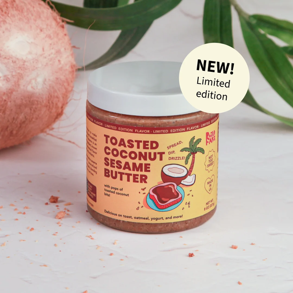 Jar of toasted coconut sesame butter with a 'NEW! Limited edition' label, surrounded by coconut pieces and leaves.