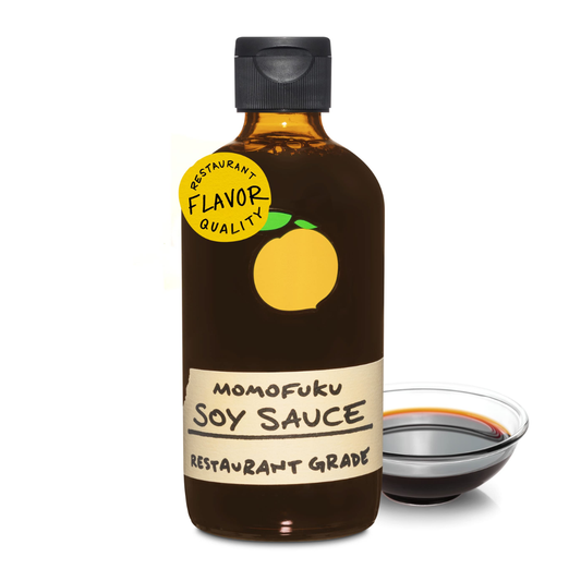 Bottle of Momofuku Soy Sauce with a small bowl of soy sauce on a white background