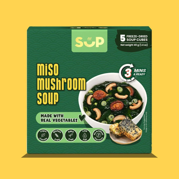 A box of SUP Miso Mushroom Soup freeze-dried cubes, featuring a dark green packaging design with yellow text and an illustration of a bowl of prepared soup, set against a solid yellow background.