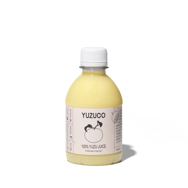 A bottle of Yuzuco 100% Yuzu Juice with pale yellow liquid, a white cap, and a white label featuring a black fruit illustration, set against a plain white background.