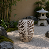 Decorative zebra-patterned urn in a garden setting with rocks and bamboo.