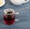 tea strainer being used to pour tea into a glass cup