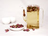 Loose tea- Pink rose on a plate next to glass pot